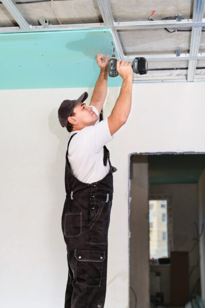Worker assembles a suspended ceiling with plasterboard and attaches the plasterboard to the metal frame of the ceiling using an electric screwdriver.